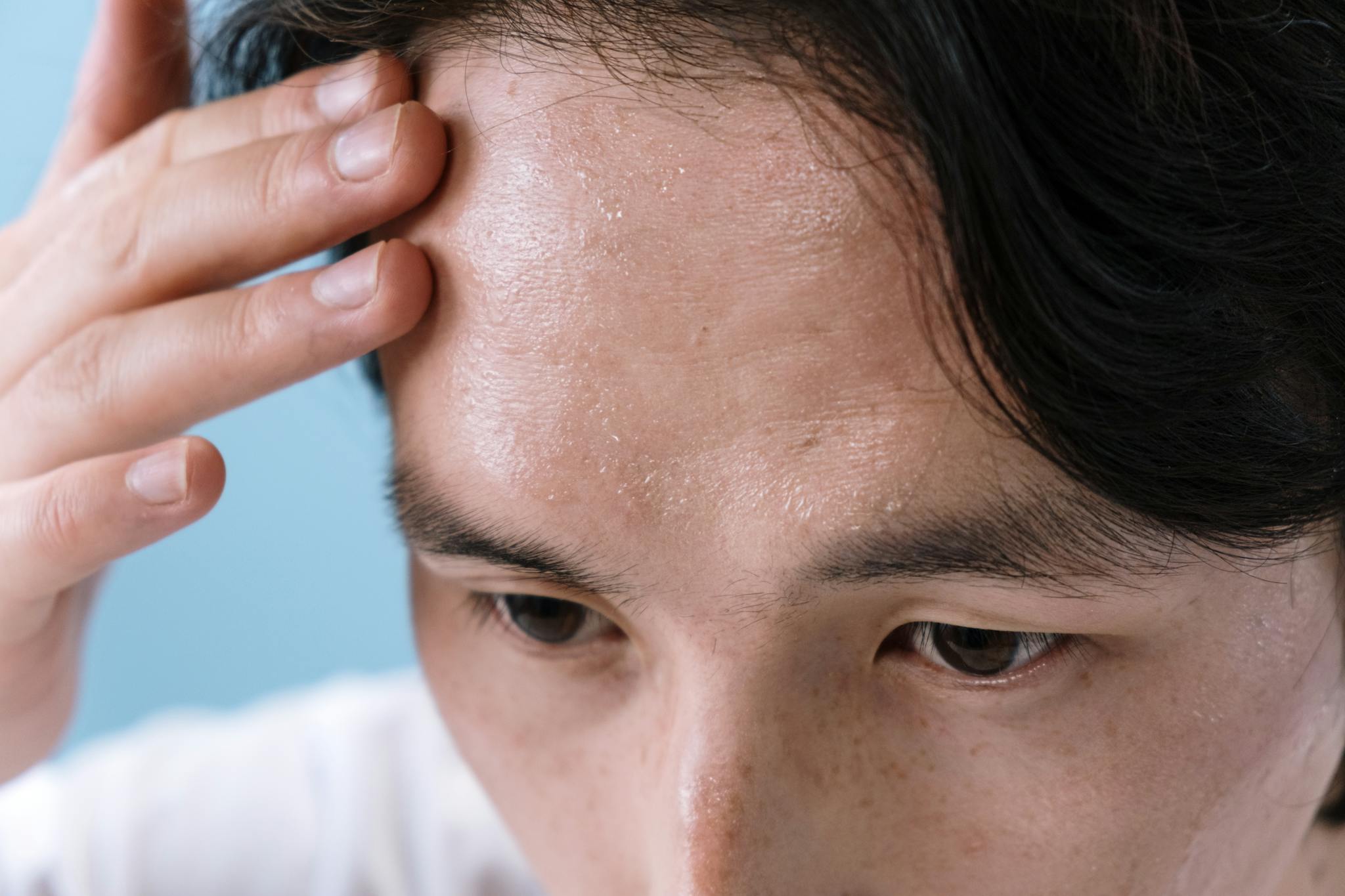 Close-up of a man with sweat on his forehead, touching it with his hand, conveying stress or illness.